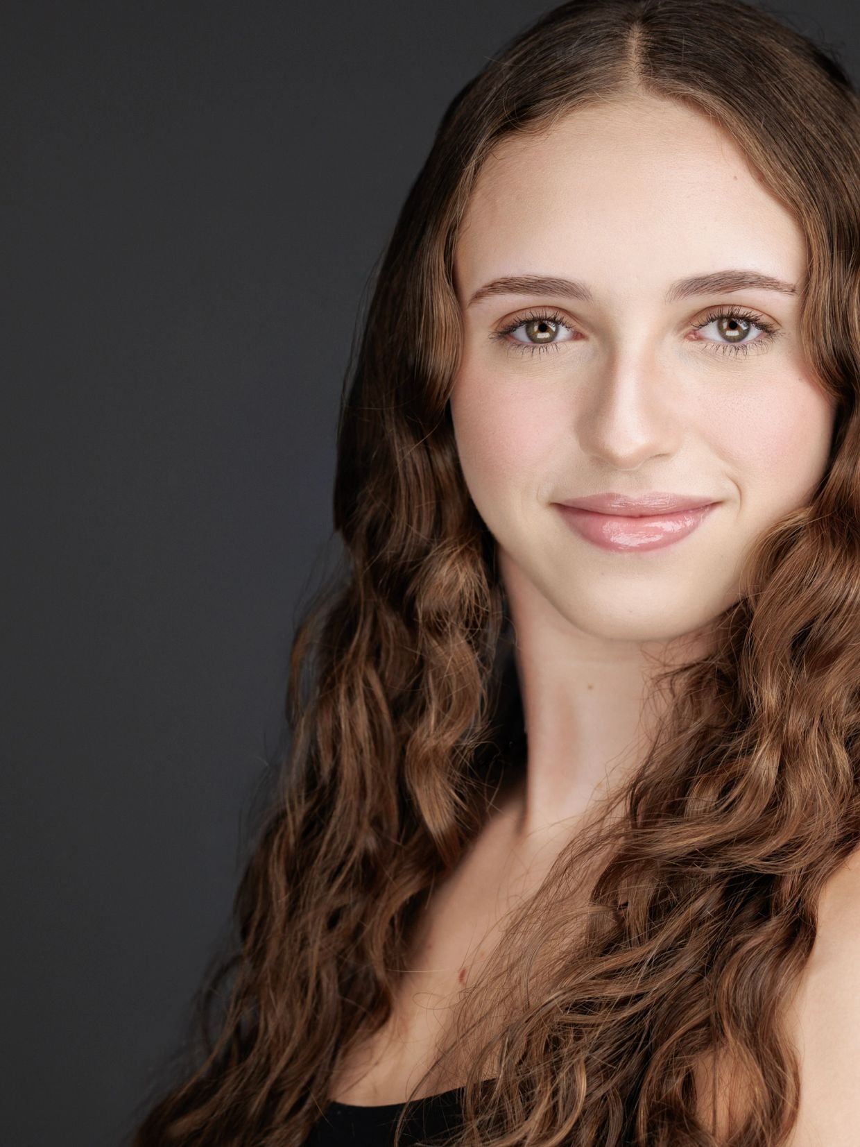 Young woman with long wavy hair smiles gently against a dark background.