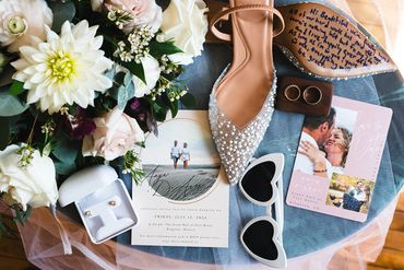 Flatlay with shoes, intive, glasses, rings, and a bouquet.