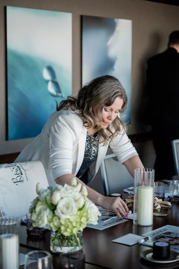 A planner in a white jacket, setting a table with personalized decor items and florals.