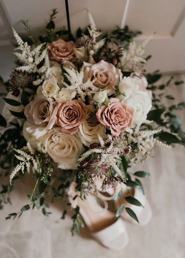Bouquet in cream, blush and greens with white wedding shoes peaking out.