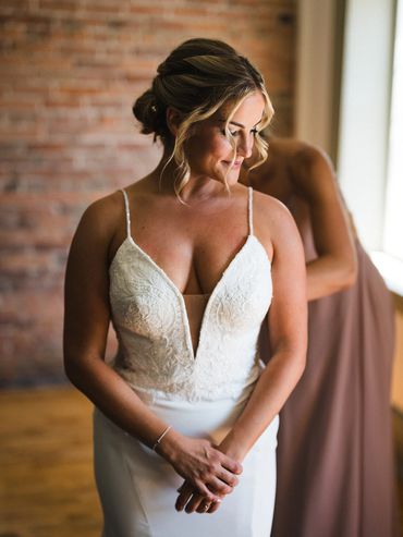 Bride pausing in front of a red brick wall while her mom does up her dress