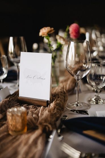 Wine glass, table number, gold votive, flowers and parts of a place setting.