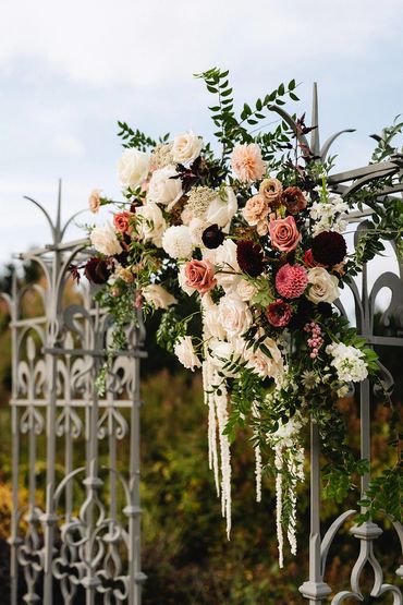 Gorgeous florals in cream, dusty rose, and burgundy secured to decorative iron fence.