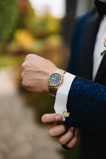 Groom wearing a blue suit and a gold watch puts on his cufflinks.