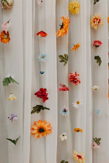 Colourful wedding flowers hanging by a string in front of white sheers and a brick wall.