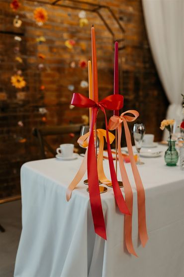 Tall taper candles in fuchsia, pink and orange with long matching bows on the sweetheart table.