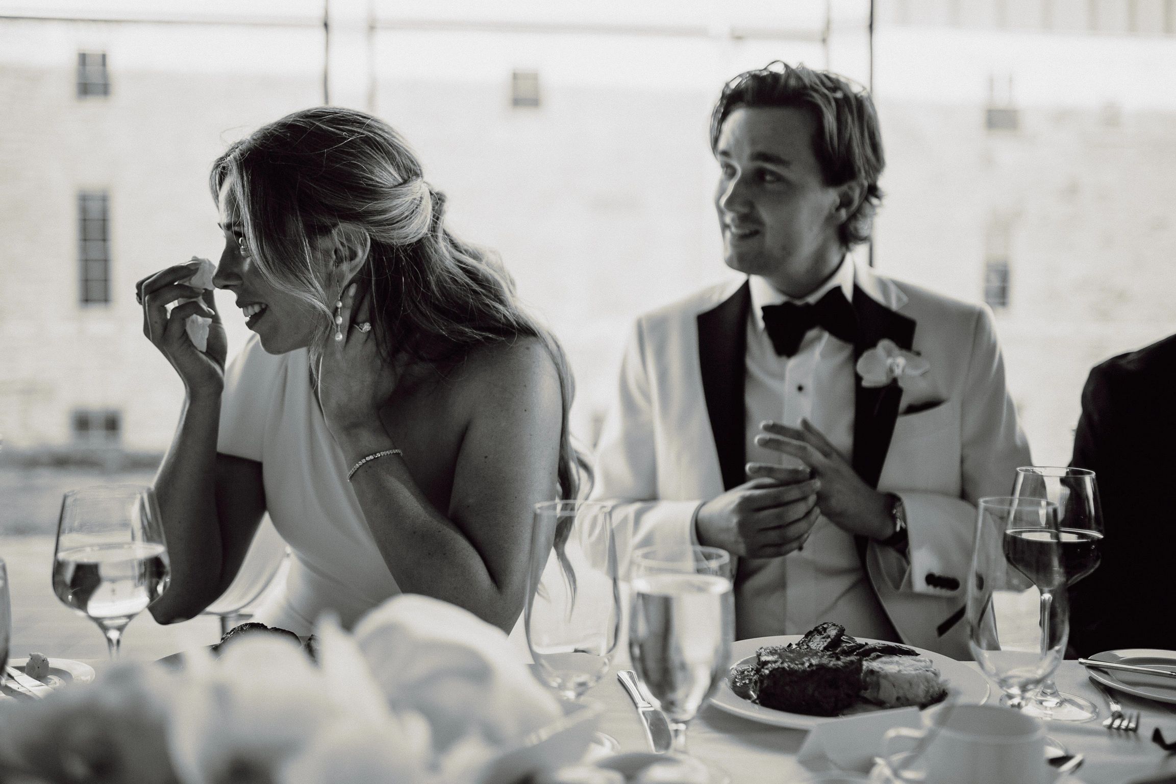 Bride wipes tears away as she and her new husband listen to speeches during dinner.