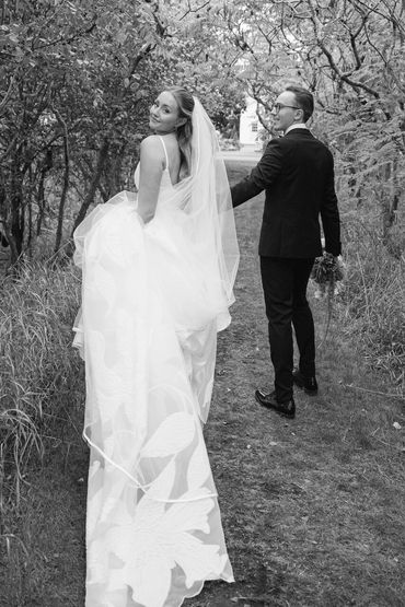 Black and white photo of bride and groom frolicking in a sumac path of trees.