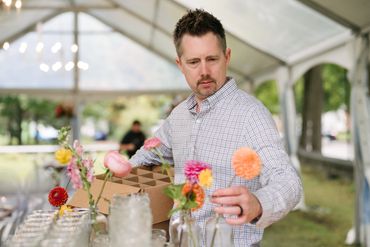 Male assistant setting out clear bud vases with multi colored coral florals.