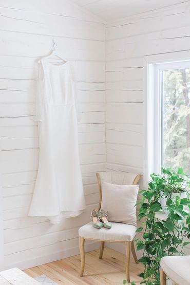 Weddind dress hanging on a while shiplap wall with a victorian chair and a trailing green plant.