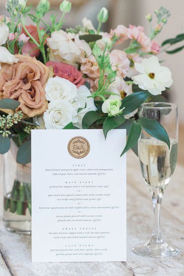 Dinner menu with a gold seal on top with a champagne glass and flowers in coffee, cream and rose.