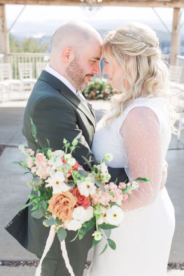 Couple forehead to forehead, embrasing while she hold a bouquet.