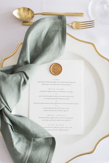 Place setting with gold cutlery, white and gold charger and sage green linen napkin