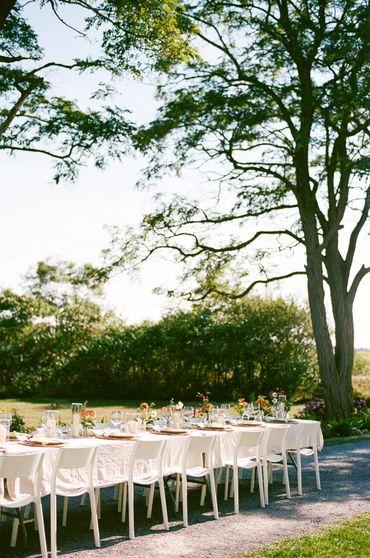 Alfresco dining in the driveway with one long dining table and white chairs.