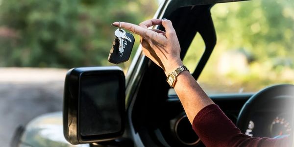 A person holding keys on her finger outside the window of a vehicle.