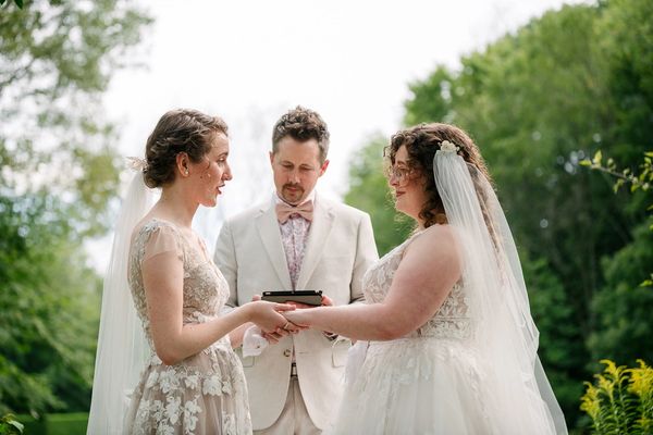 Brides saying their vows while the officiant in beige pauses at Spindle Tree Manor