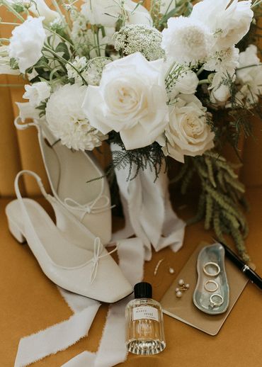 Flatlay with white flower, white shoes, jewlery, perfum and a pretty shell tray.