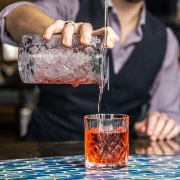 Bartender straining a red cocktail into a decorative glass.
