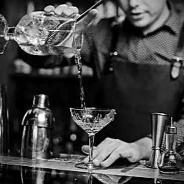 Bartender pouring a cocktail through a strainer into a glass.