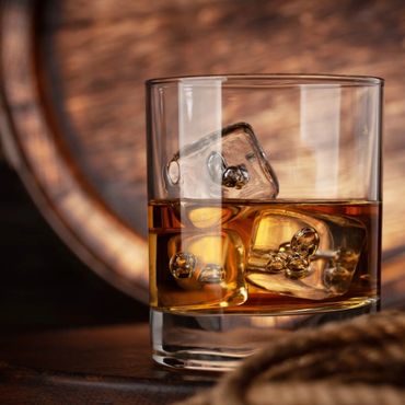 Whiskey glass with ice cubes in warm, rustic setting.