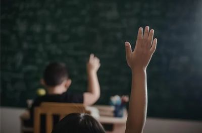 Students raising their hands in a classroom.
