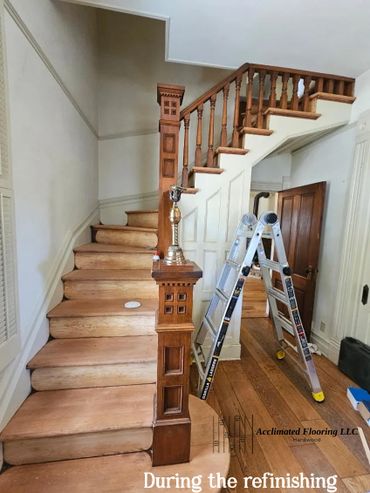 Wooden staircase undergoing refinishing with a ladder nearby.