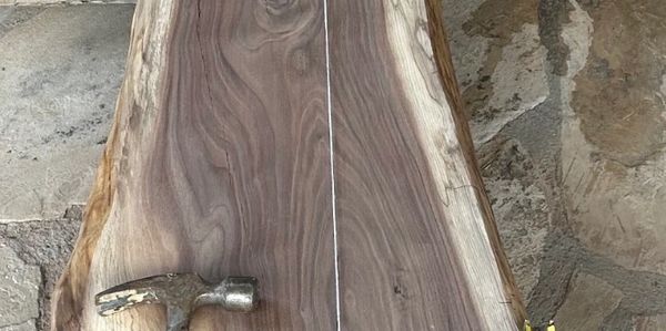 A hammer resting on a large, polished wooden slab with a stone floor background.