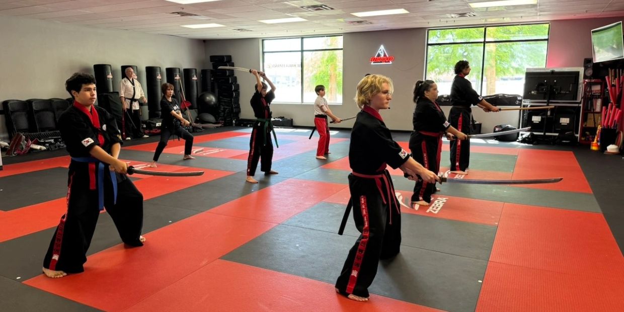 Martial arts class practicing sword techniques in a dojo with students and instructor.
