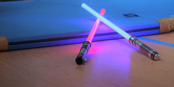 Two combat sabers lean up against a training mat on the floor. One is red and the other is blue.