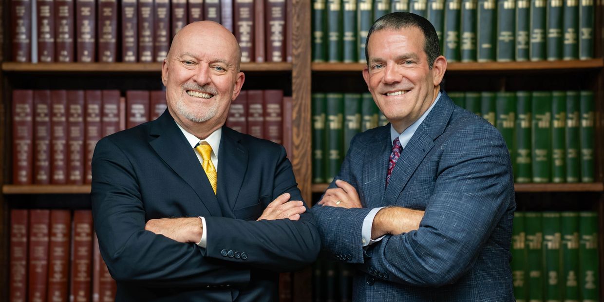 Two men in suits smiling with arms crossed.