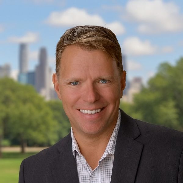 Smiling man in business suit with city skyline and park background.