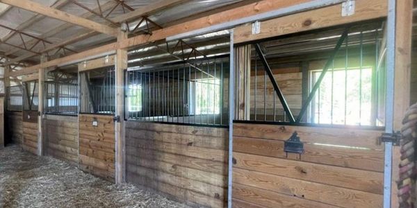 Empty wooden horse stalls in a barn with metal bars and hay on the floor.