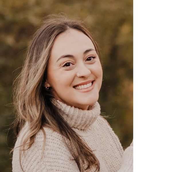 A woman smiles warmly wearing a cozy beige knit sweater outdoors.
