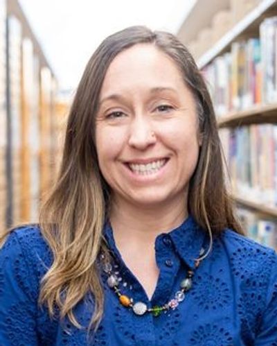 Smiling woman in blue shirt standing in a library aisle.