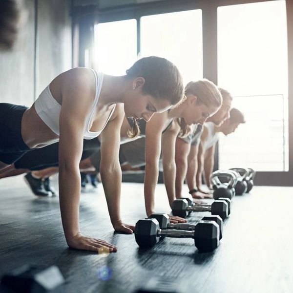 Group fitness class doing push-ups with dumbbells in a bright gym.