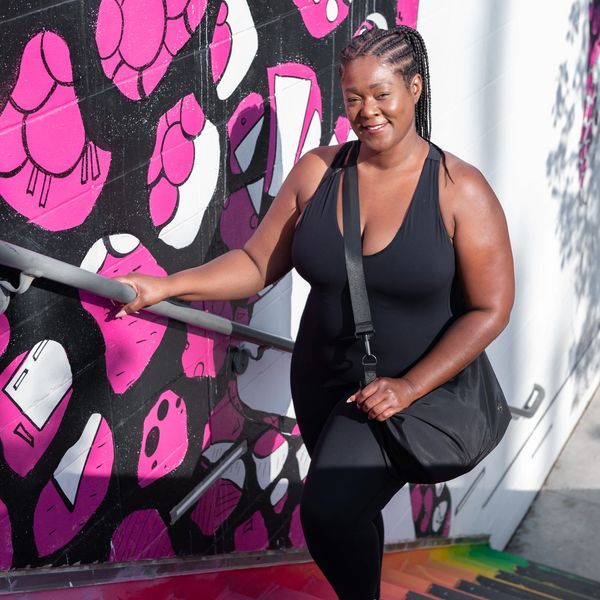 Woman in black outfit smiling on colorful stairs next to vibrant mural.