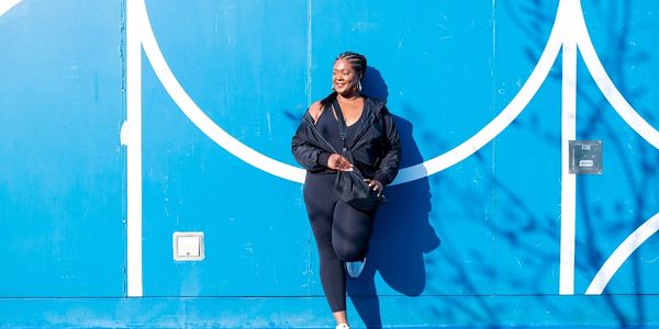 Woman in black activewear leaning against a blue basketball court wall.