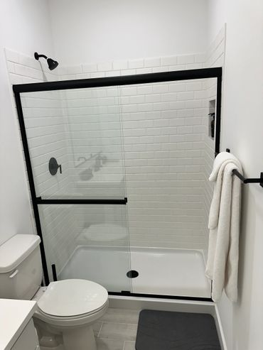 Modern bathroom with black-framed glass shower and white tiles.