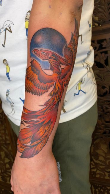 Vibrant phoenix tattoo with a blue moon background on forearm.