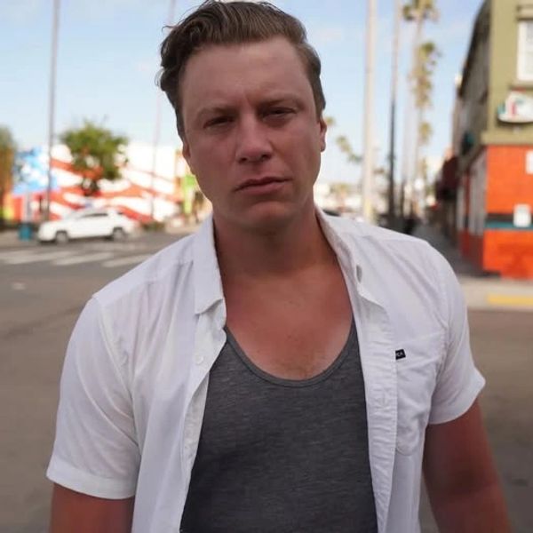 Man with a serious expression standing on a sunny street.