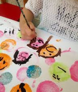 A child painting colorful faces on paper with a brush.