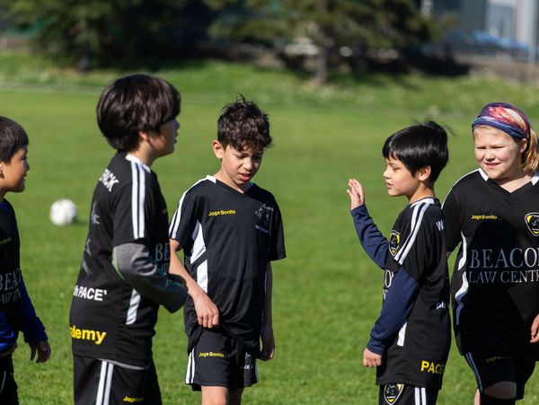 Young boys in black soccer uniforms stand on a grassy field.