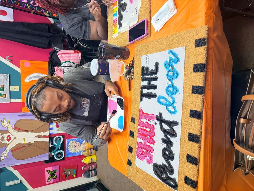 Man painting a colorful sign that says 'SHUT THE front door' at a vibrant art studio.