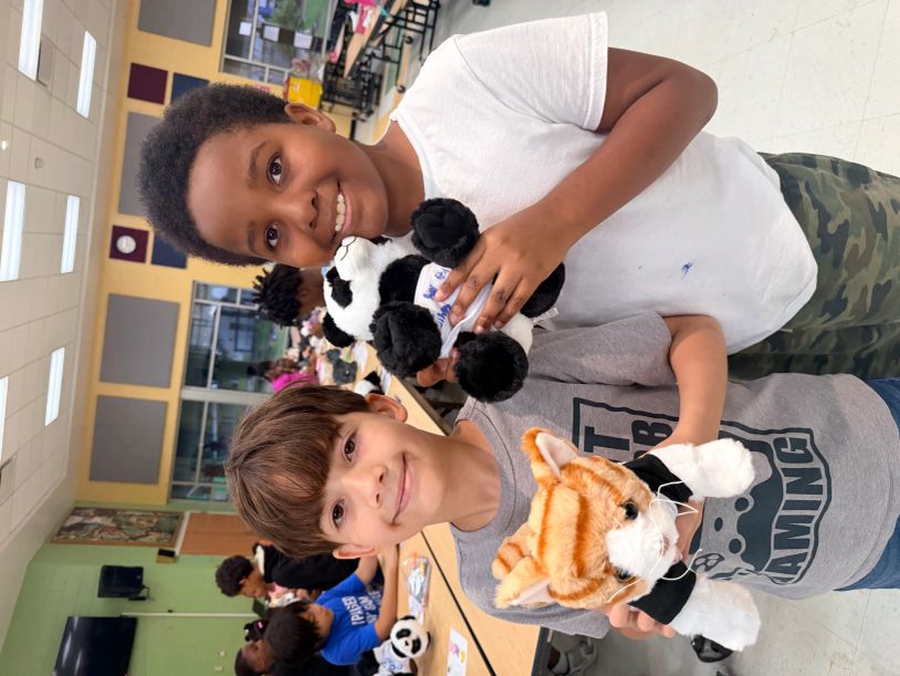 Two boys smiling, holding stuffed animals in a classroom.