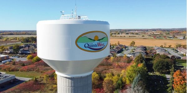 Water tower with Quinte West logo in a rural area.