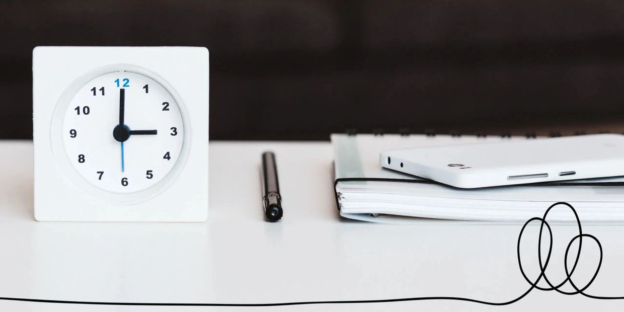 A minimalist desk setup with a clock, pen, notebook, and smartphone.
