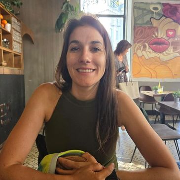 A smiling woman sitting at a cafe table indoors.