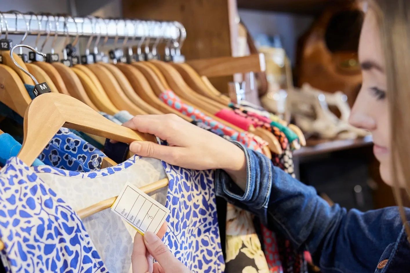Woman examining price tag on a blue patterned dress in a clothing store.