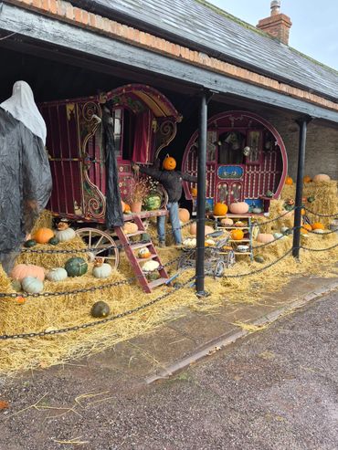 Halloween-themed display with pumpkins, hay, and spooky figures around traditional gypsy wagons.