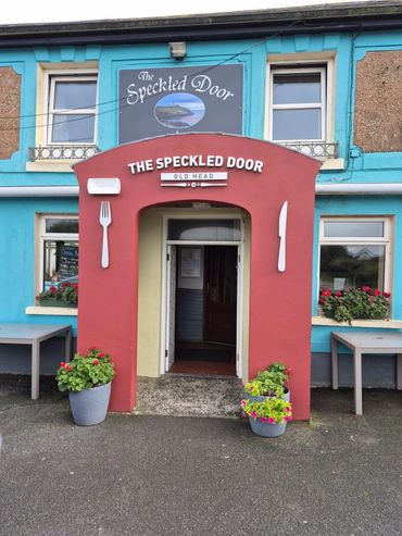 Entrance to The Speckled Door restaurant with colorful exterior and flower pots.